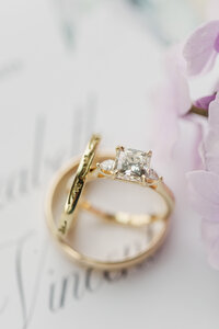 close up of wedding rings sitting on top of a wedding invitation