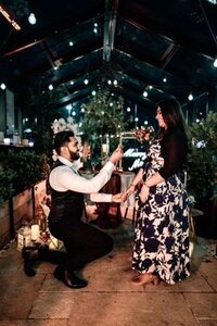 Jasneet proposing to Shayal inside a styled glasshouse with candles, florals, and romantic dinner table setup, photographed by Auckland proposal photographer Zanthe Vorsatz.