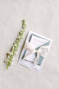 wedding detail flatlay invitatation suite set with white silk bow fresh florals on flatlay styling mat