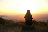 Women enjoying a sunset as she sits on a rock