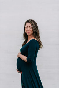 A stunning mother wearing an evergreen maternity dress holding her belly