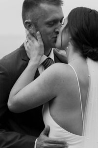 A newlywed couple with their arms around each other kissing 
