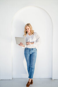 Kristin Jacob newborn sleep coach standing against arched wall with computer