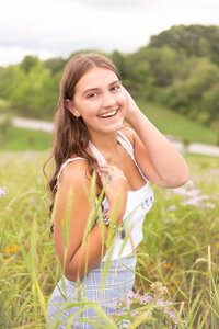 High school senior girl standing in field of tall grasses laughing