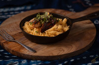 A bowl of salmon pasta garnished with fresh herbs and vibrant vegetables, beautifully arranged on a black table.