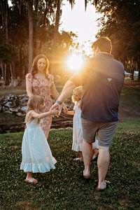 Two young sisters in white dresses laying in a field of wildflowers, smiling and playing during a golden hour family photography session in Gainesville, Florida by Salt + Heart Photography
