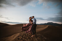 man and woman in pink dress kiss in great sand dunes national park 