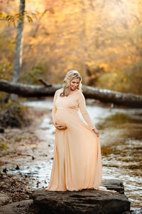 Beautiful mother poses in front of a creek in the fall near Birmingham