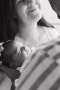 Mother gazing down at her newborn baby wrapped in a blanket, with soft window light falling on them.