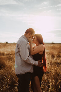 a couple hugging foreheads, touching women's hands on man's face, sunset in the background at a golden field    