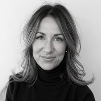 CEO of Sweet Pea Ink Creative with shoulder-length brown hair, wearing a black shirt stands against a plain white background—an effortlessly stylish look, perfect for the creative minds at Sweet Pea Ink Creative specializing in brand design.