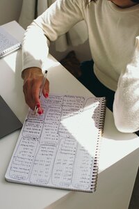 Kaya with pen in hand hovering over a notebook filled with handwritten notes at a white desk