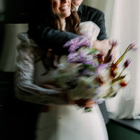 Blurry close up image of groom's arms wrapped around bride with her bouquet in front of them