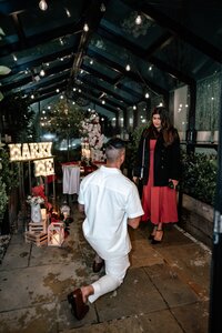 Evening glasshouse proposal for Harneet and Simmeran with glowing “Marry Me” light sign and romantic red floral décor, photographed by Auckland proposal photographer Zanthe Vorsatz.