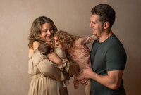 In-Home newborn session family photo with eldest daughter kissing little sister and parents smiling