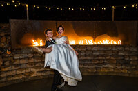 Bride and groom embracing in front of a glowing fireplace at night during their Colorado wedding at Marchand Ranch.
