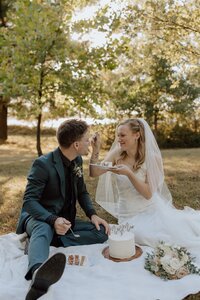 bride and groom having a picnic in the grass eating cake