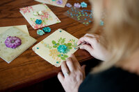 A woman's hands designing a custom handmade card with flowers and gems on it.
