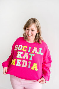 Kat Murphy in a pink Social Kat Media sweatshirt in front of a white wall