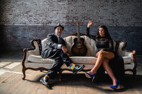 Two people sitting on a couch with a guitar in between them 