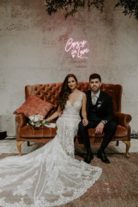 M&C Posing on a velvet couch with a neon sign above.