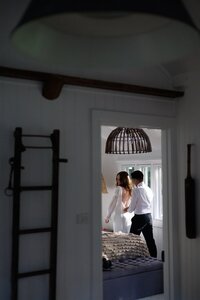 A man zips up a woman's dress, framed through a doorway, representing the artistic style of photographer vendors at the Crush Collective wedding show.