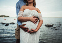 a man standing behind a woman with their arms intertwined around her pregnant belly