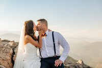 a couple is sharing a kiss, she's wearing a veil and he has a bowtie with suspenders on