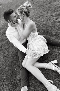 Black and white engagement photo of couple sharing a quiet kiss on picnic blanket.