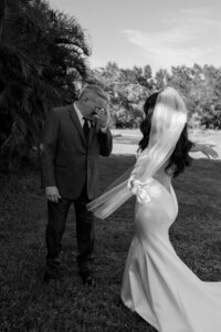 Emotional black and white photo of a father wiping tears during a heartfelt first look with his daughter in her wedding gown at Tree House Venue in Vero Beach, Florida.