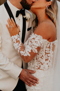 A detailed shot captures the bride and groom, dressed elegantly, sharing a tender kiss and embracing each other with love.