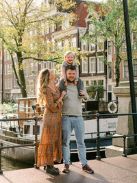 A toddler boy sits on his father's shoulders while his mother smiles at him in the Jordaan area of Amsterdam. 