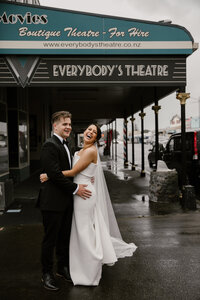 Bryce and Sarah standing outside everybodies theatre in new plymouth during their wedding photoshoot