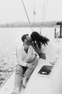 A person leaning down to kiss their partner sitting on a sailboat 