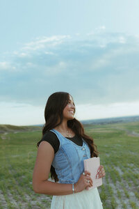 A portrait of a missionary about to leave for her mission. She's holding a pink Book of Mormon to her stomach and looking off to the side.