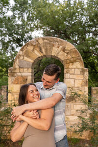 Couple hugs and laughs in front of stone archway.