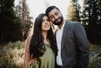 jackson hole photographers photographs outdoor engagement session in the tetons with man in a suit and woman in a dark green silk dress as they stand together in the woods
