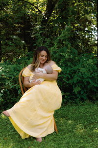 woman holding a baby while sitting in a chair outside next to trees
