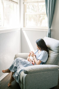 mom rocks sleeping baby by window in nursery