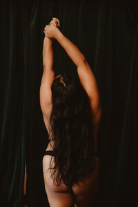 View from behind of a person with their hands up and their hair flowing down their back 