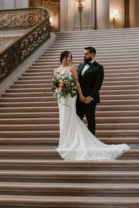Bride and groom on grand staircase of San Francisco City Hall.
