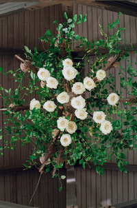 green leaves and vines in a circle with white flowers on top hanging on the wall. 