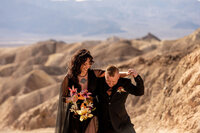 A bride in a black dress walking on the vast, white salt flats of Death Valley, her figure standing out against the expansive desert horizon.