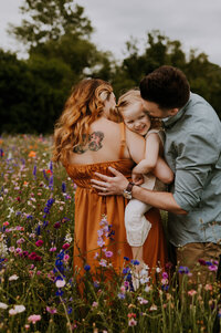 A mom holding her daughter on her hip while dad kisses her on the cheek at Crowley Park in Richardson, Texas