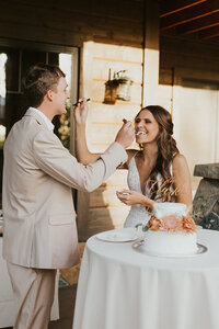 Adriana Montoya Photo, wedding photographer in Rexburg, Idaho. A bride kisses her groom on his cheek while he cuts their wedding cake at their wedding reception.