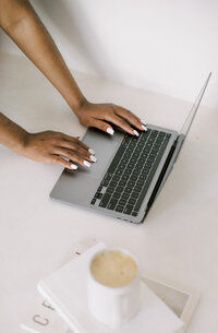 Woman types on her silver laptop working on her creative business website template.