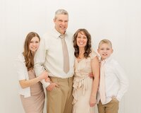 Family, who make up the JHP Team, with their arms around each other by a white wooden wall.