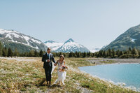 a couple running through a wildflower field in alaska on their elopement day by a lake and with mountains