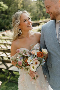 Black and white wedding photo of a bride and groom celebrating during their wedding reception. They are both wearing heart-shaped sunglasses with their initials written on the lenses. They are holding drinks and smiling. The bride is on the right and is holding her hand up in their air with excitement. The groom is on the left and is smiling and embracing her.