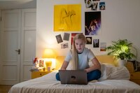 Student sits crosslegged on bed with laptop studying.